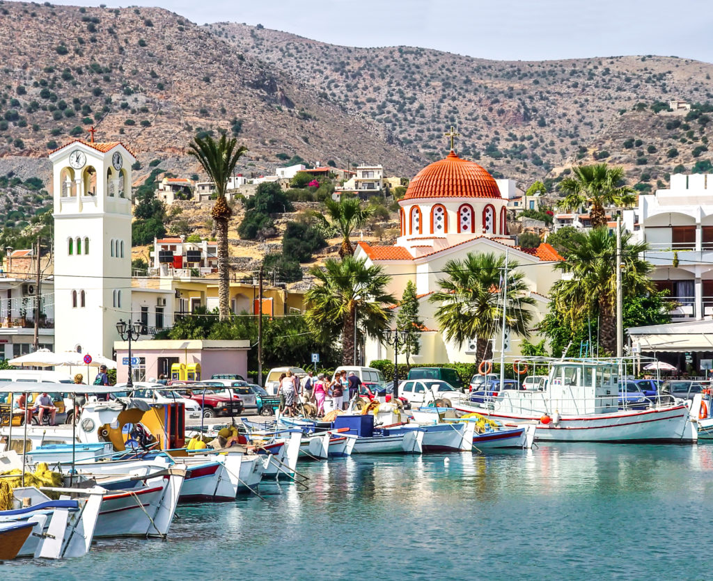 Greek church and fish boats in a little port. Imposing mountains at the back.